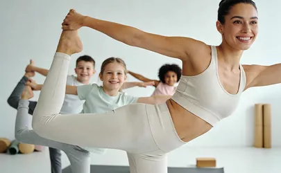 Eine Yogalehrerin macht eine Yoga Figur vor den Kindern in ihrem Kurs