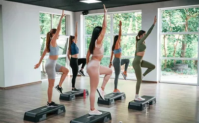 Eine Gruppe von Frauen beim Step Aerobic auf Steps in einem Studio mit großen Fenstern