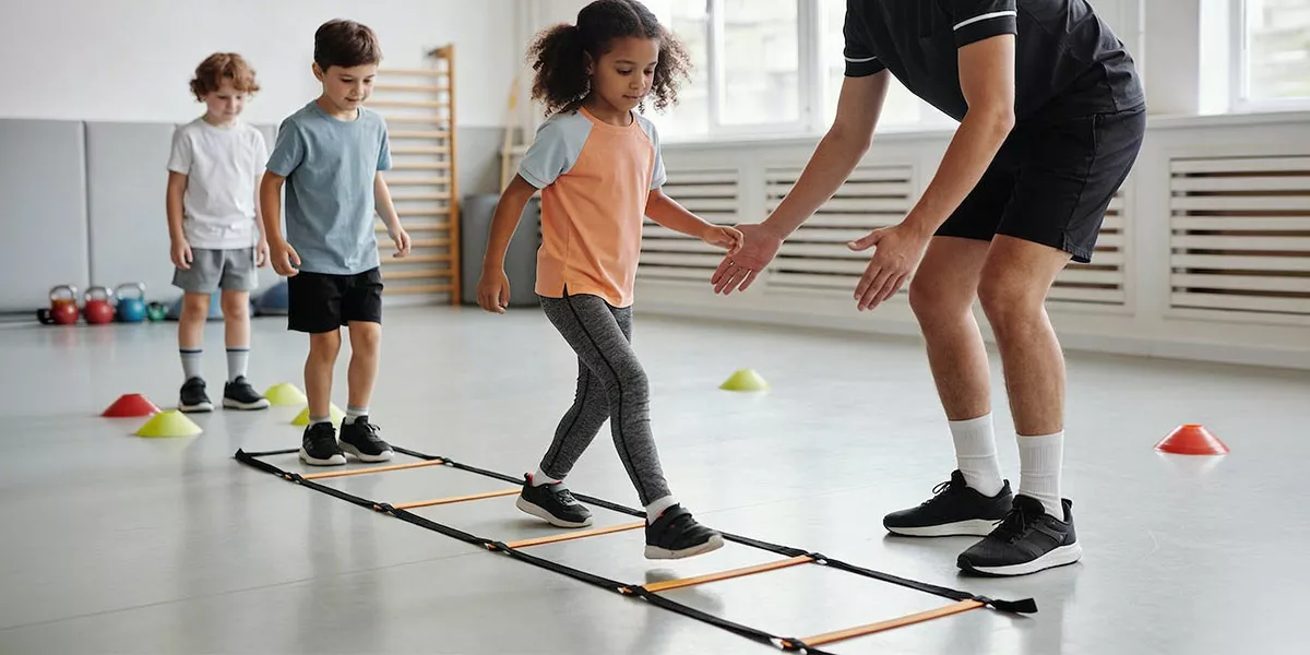 Eine kleine Gruppe von Kindern macht Übungen auf einer Speed Ladder mit ihrem Trainer