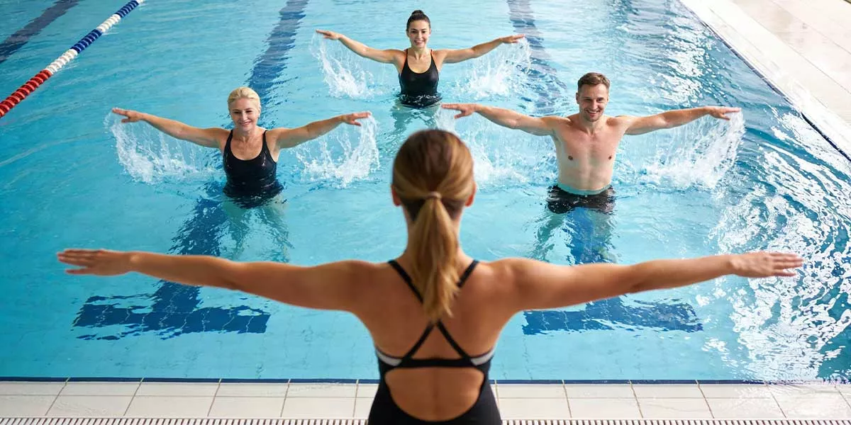 Eine Aquafitness Trainerin leitet vom Beckenrand eine Gruppe in einem Schwimmbecken an