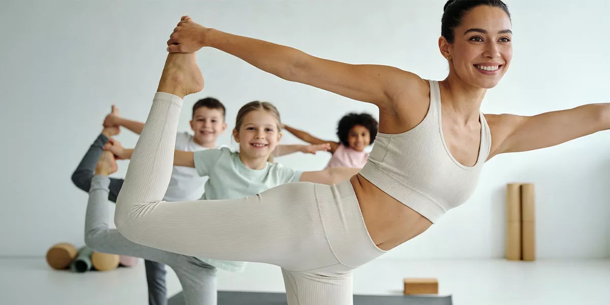 Eine Yogalehrerin macht eine Yoga Figur vor den Kindern in ihrem Kurs