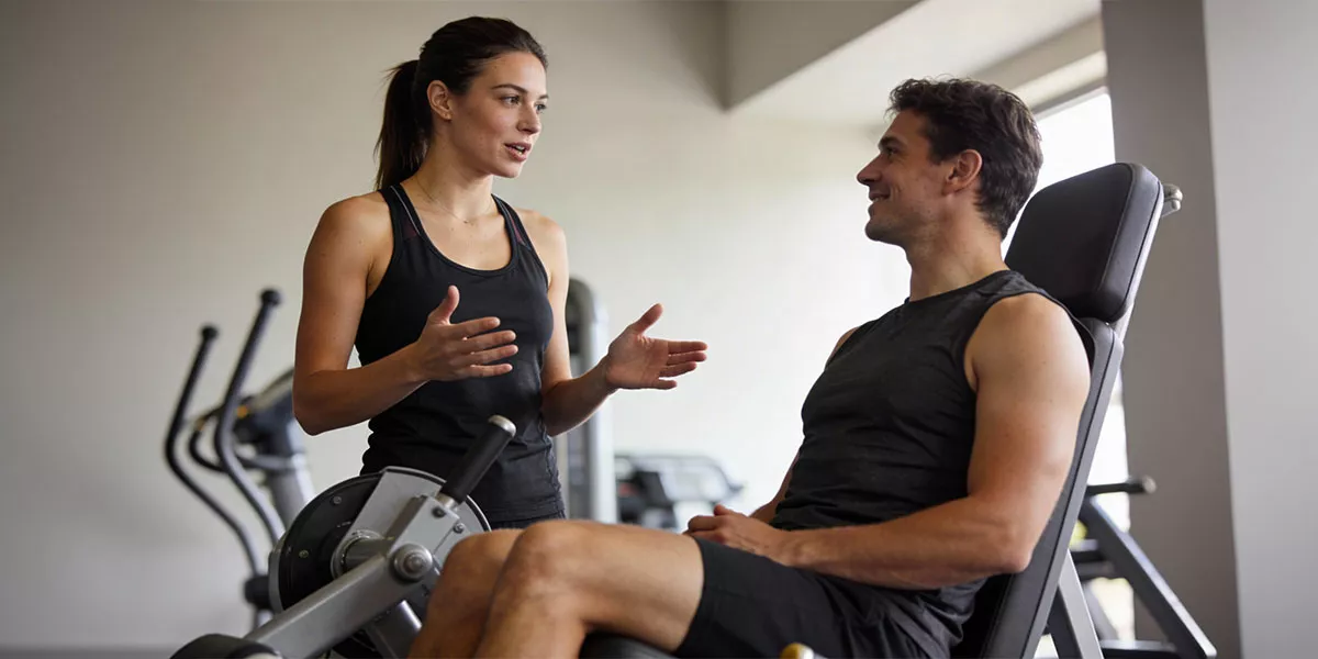 Eine Fitnesstrainerin beim Training am Gerät mit ihrem Kunden in einem schlichten Studio