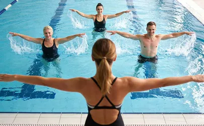 Eine Aquafitness Trainerin leitet vom Beckenrand eine Gruppe in einem Schwimmbecken an